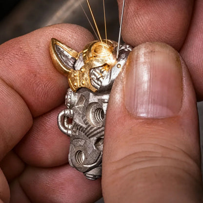 Hands working on a small mechanical dog component with a pointed tool.